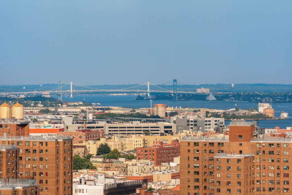 Daytime view from Maven in The Bronx overlooking city rooftops, river, & suspension bridges
